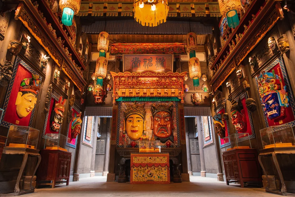 Painted masks, carved wooden beams and lanterns inside Baoren Pavilion at Xiangxi Fu